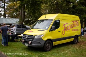 Yellow delivery vans and vehicles parked in a row at an outdoor event venue.