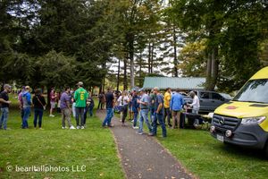 Crowd of attendees gathering on a tree-lined path at an outdoor festival.