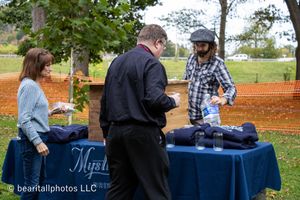 Event setup with blue-clothed tables under trees for vendor displays.