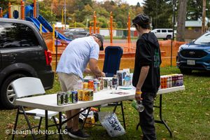 Outdoor festival area with playground equipment and vendor tables set up on grass.