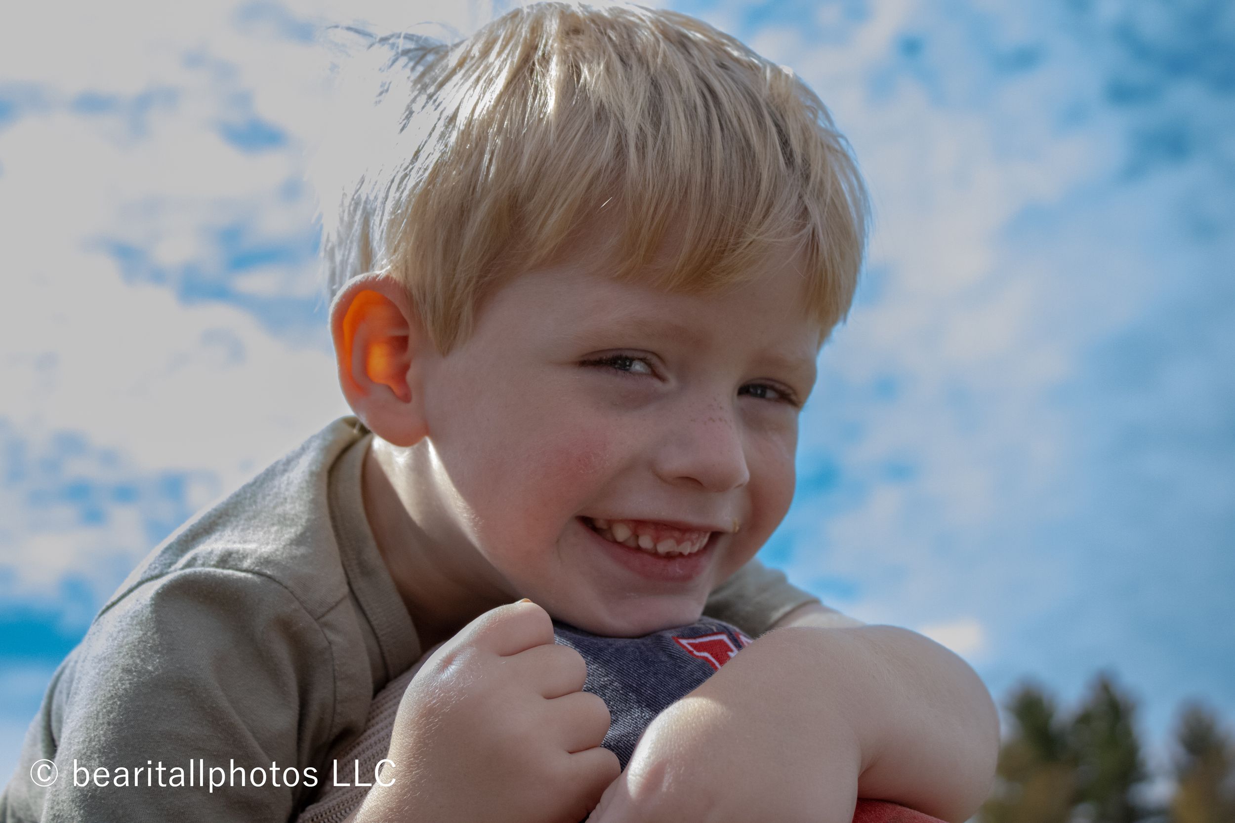Child enjoying outdoor activities against a bright blue sky with clouds.