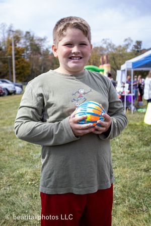 Child in green sweatshirt holding colorful toys at an outdoor event.