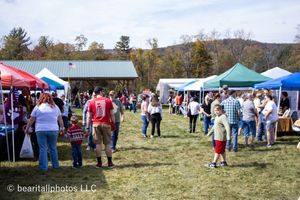 Wide panoramic view of an outdoor festival with scattered tents and attendees on grassy hillside.