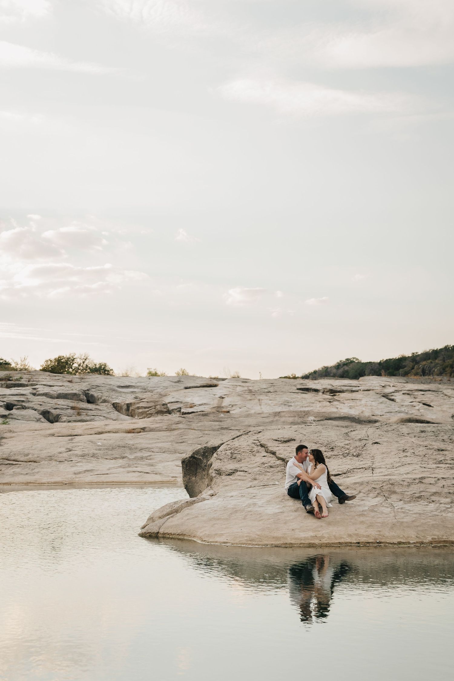A couple stands together in shallow water during a romantic photoshoot by a serene lake.