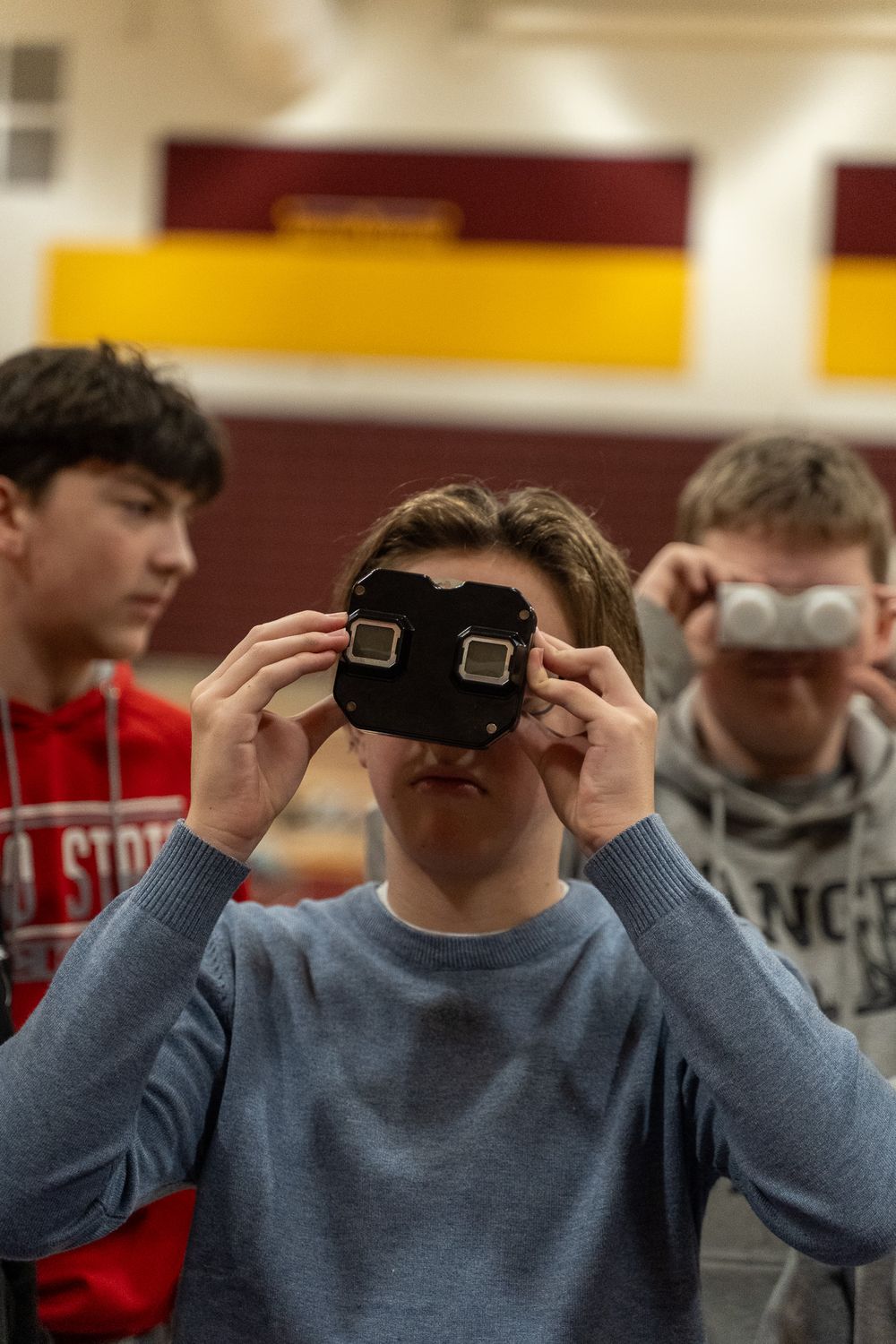 Students using View-Master stereoscope viewers in a school gymnasium during a science or technology class activity.
