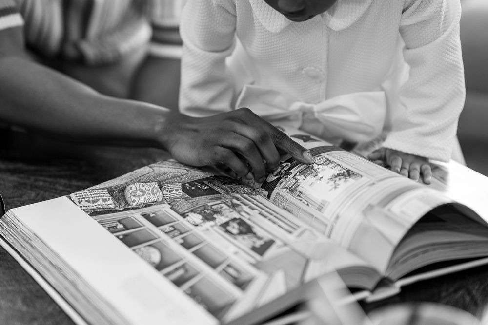 Two students in white uniforms reading a large illustrated book together in black and white photo.