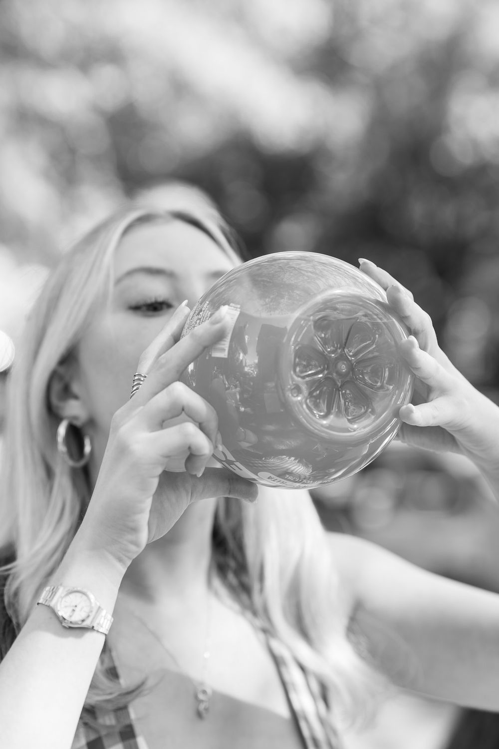 Black and white photo of a blonde woman drinking from a decorative glass jar outdoors.