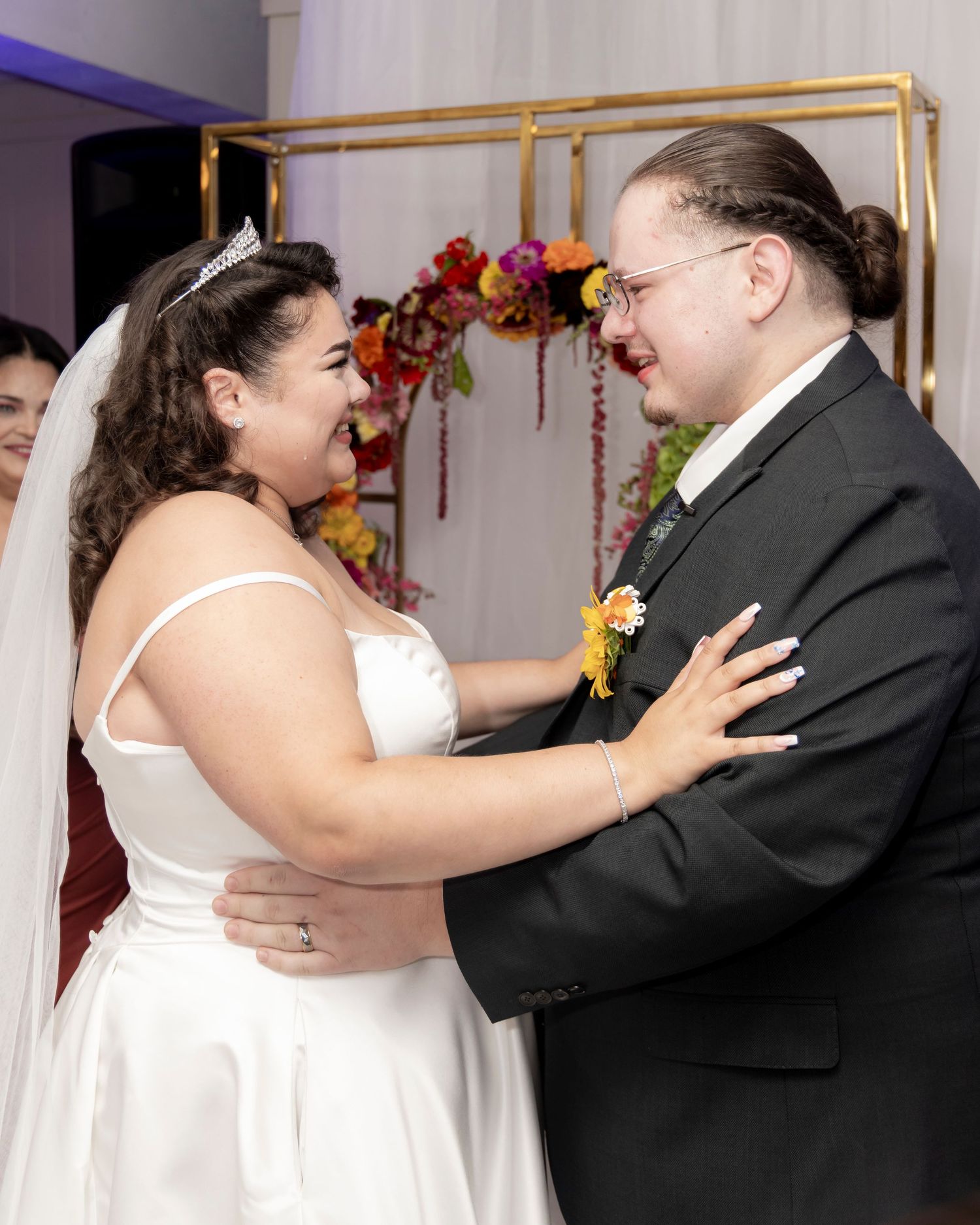 A bride and groom walk across a tiled reception hall floor with white tables and blue accent lighting visible.