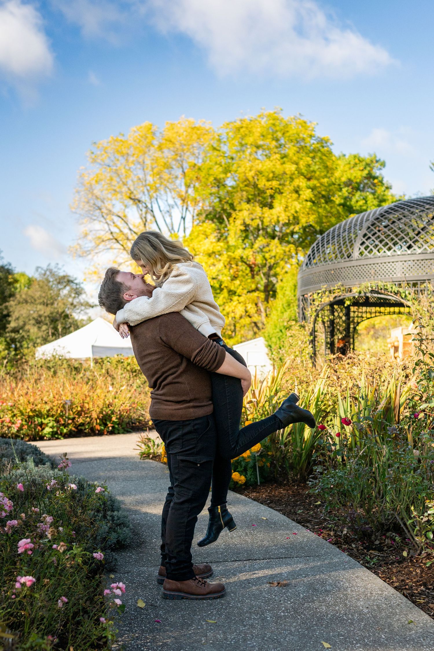 A romantic couple embraces and shares a joyful moment in a garden path surrounded by autumn foliage.