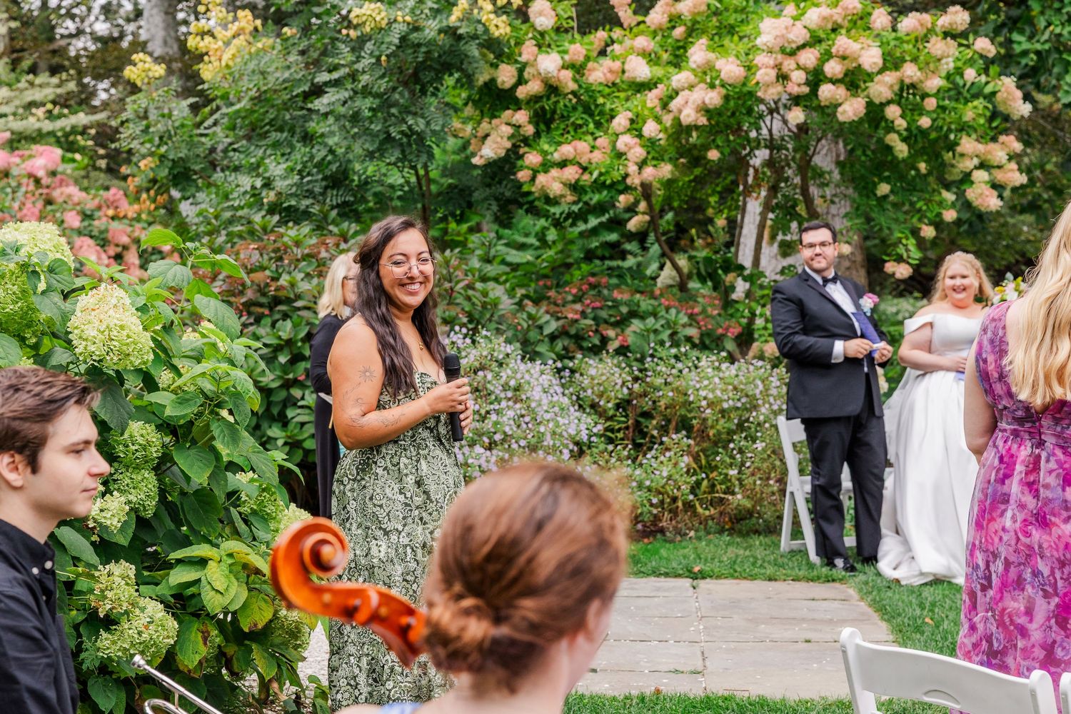 Wedding guests dance and celebrate at an outdoor garden reception surrounded by lush greenery and flowers.