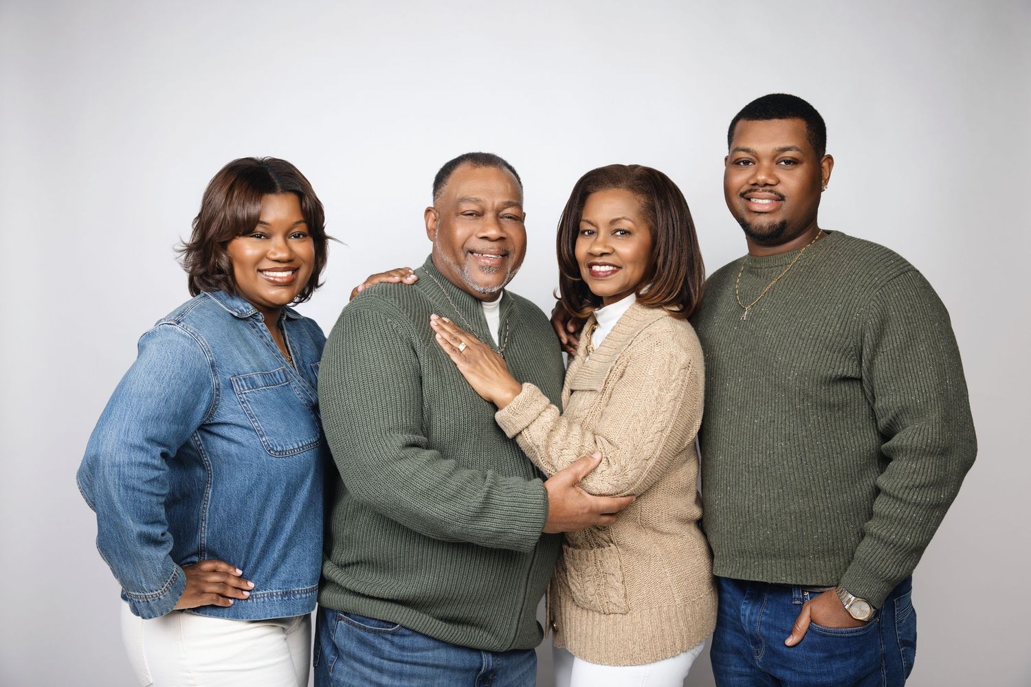 A family wearing coordinated green and beige sweaters poses together for a casual portrait session.