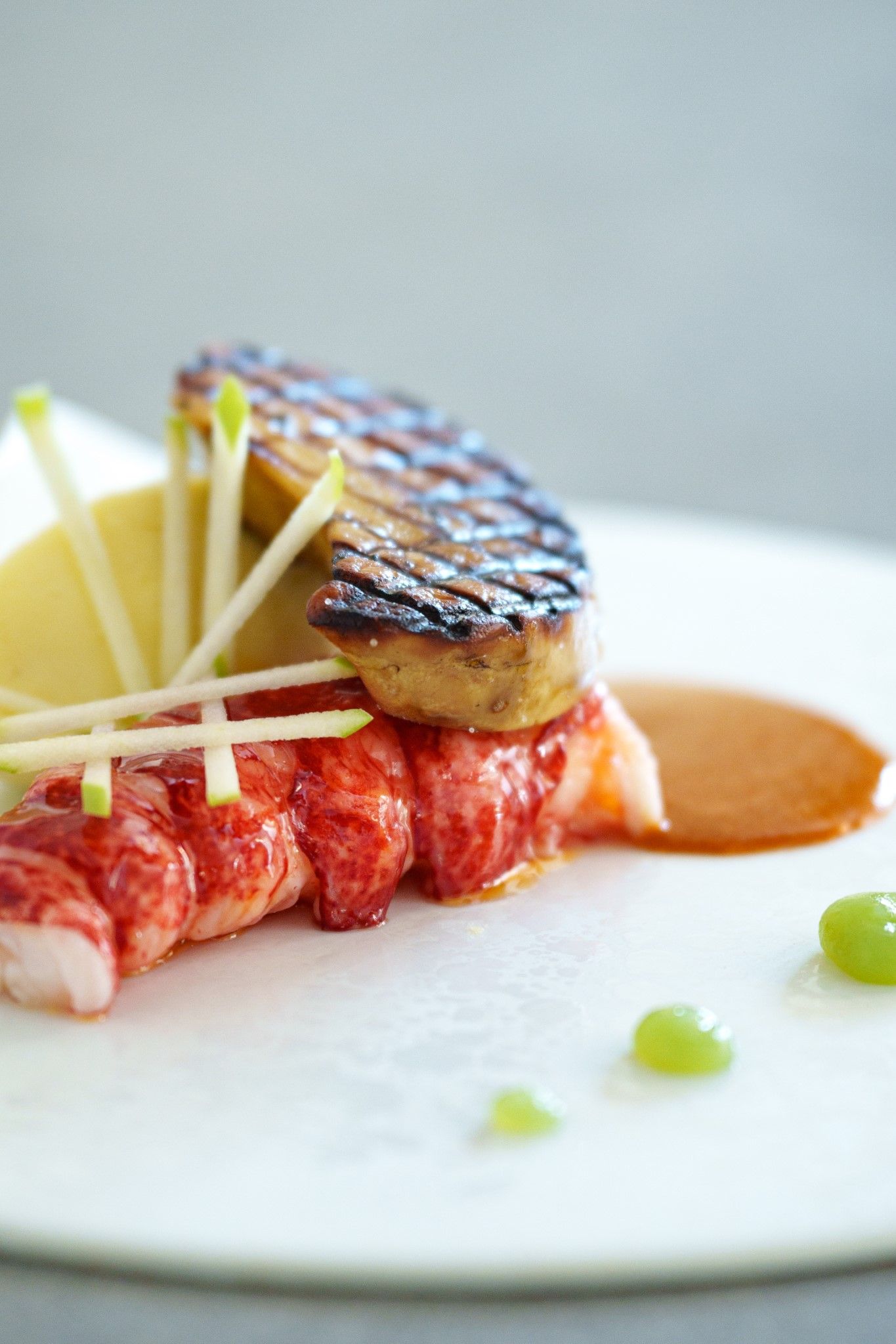 Elegant plated lobster dish with seared foie gras and apple garnish on white plate.