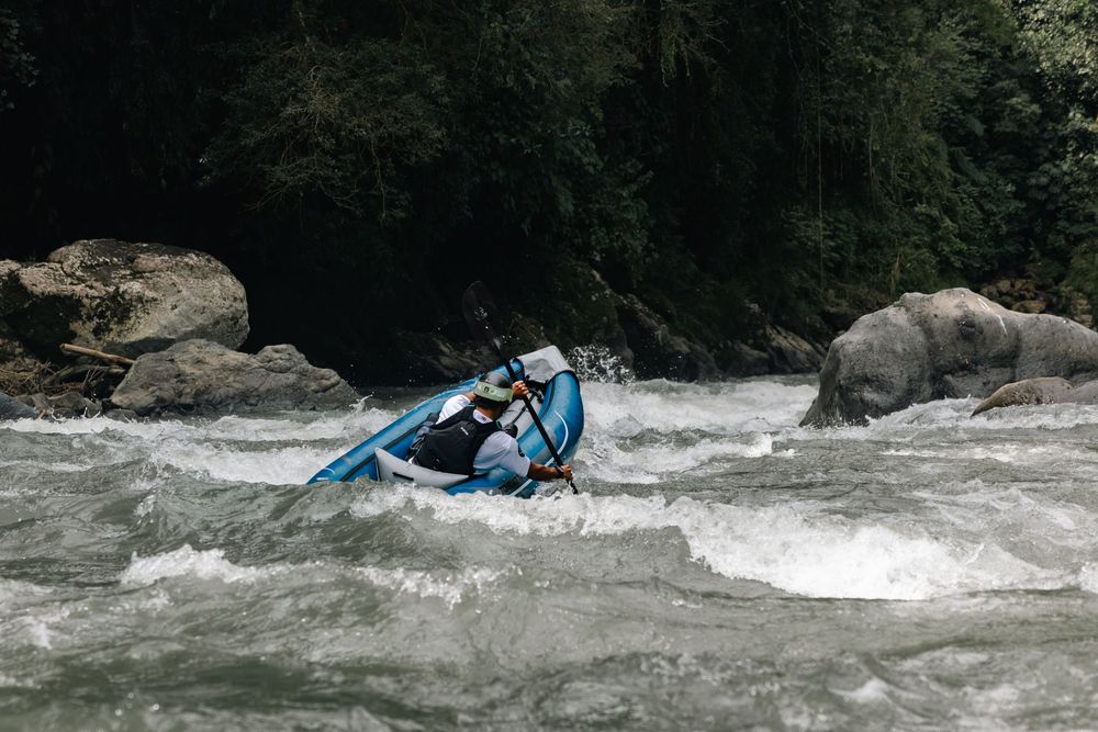 Kayakers maneuver through rocky whitewater rapids with intense water spray.