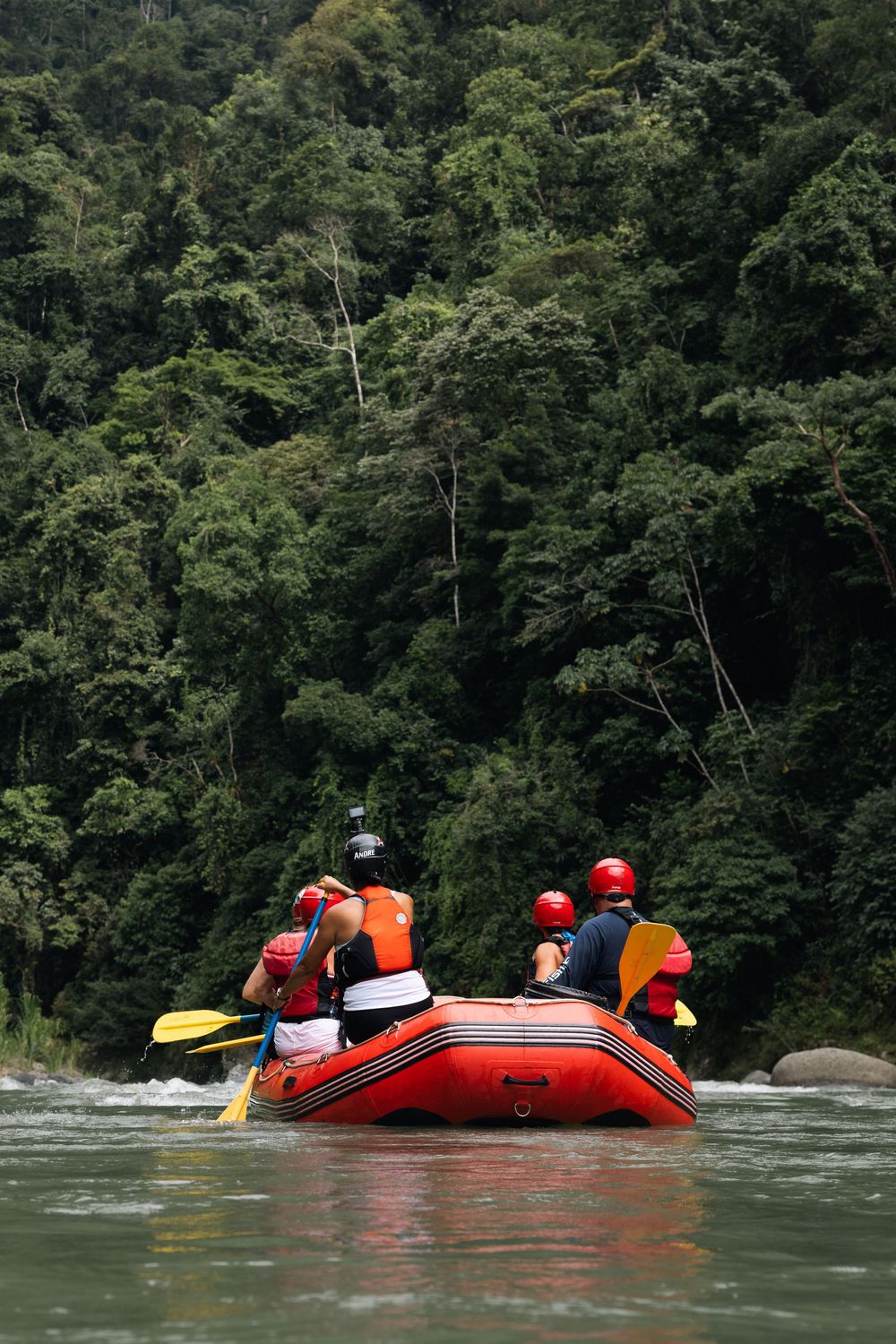 Red rafts navigate calm river waters against a backdrop of steep forested hillsides.