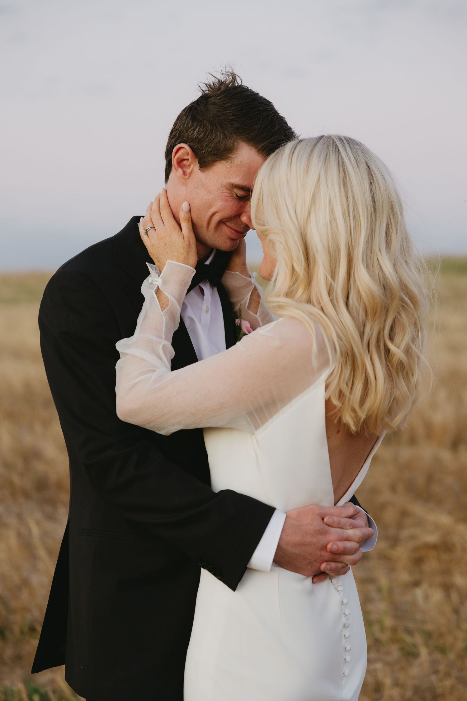 Intimate wedding couple embracing in a golden field during sunset, creating a romantic and tender moment.