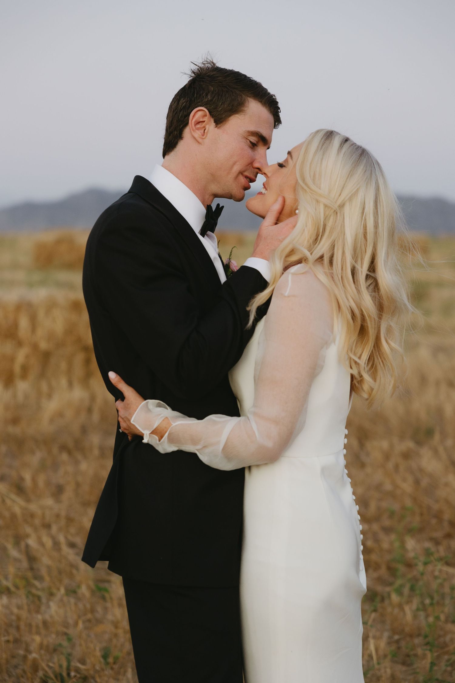 Couple in wedding attire sharing intimate moments in a golden field at sunset.