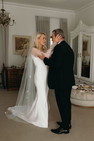 Romantic first look sequence between couple in wedding attire in an elegant white room with chandelier.