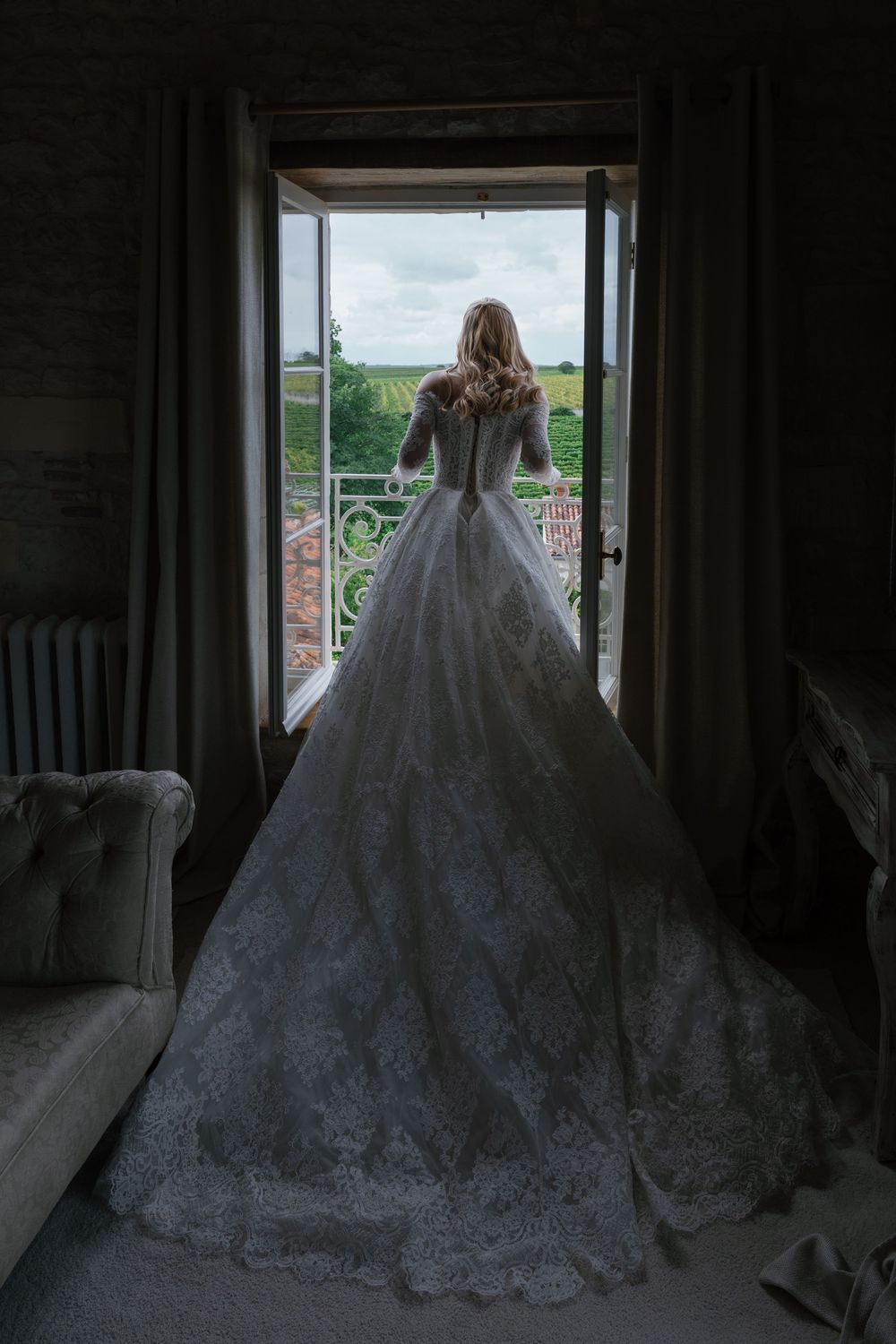Elegant wedding dress with intricate lace detailing and dramatic train photographed in a dark interior setting.