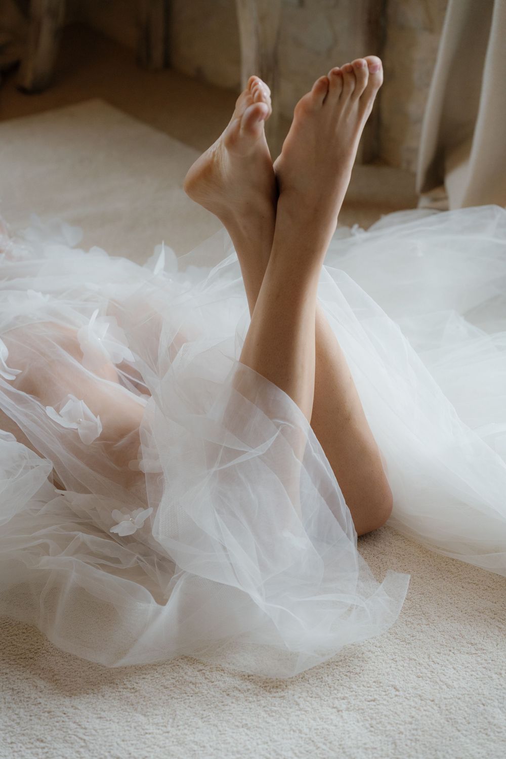 Small bare feet peek out from delicate layers of white tulle fabric against a light carpet.