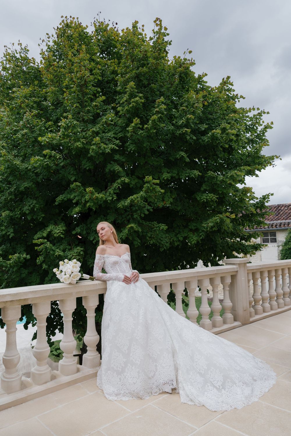 A stunning bridal portrait series on a white stone balcony with lush green trees creating an elegant backdrop.
