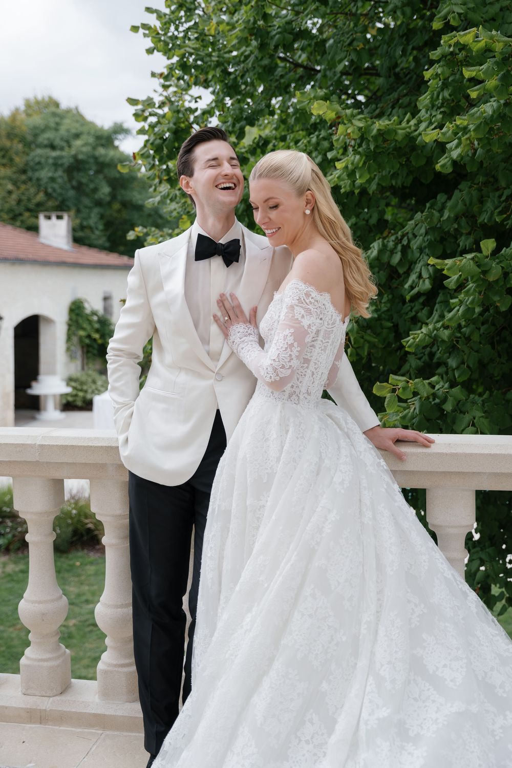 Elegant wedding couple posing on a white balcony surrounded by lush greenery.