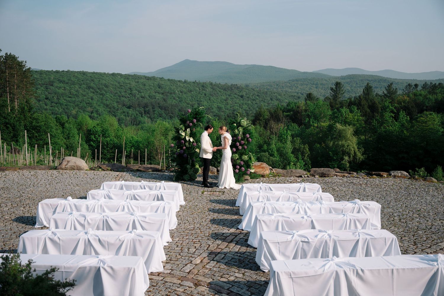 White folding chairs set up for an outdoor wedding ceremony with mountain views in the background.