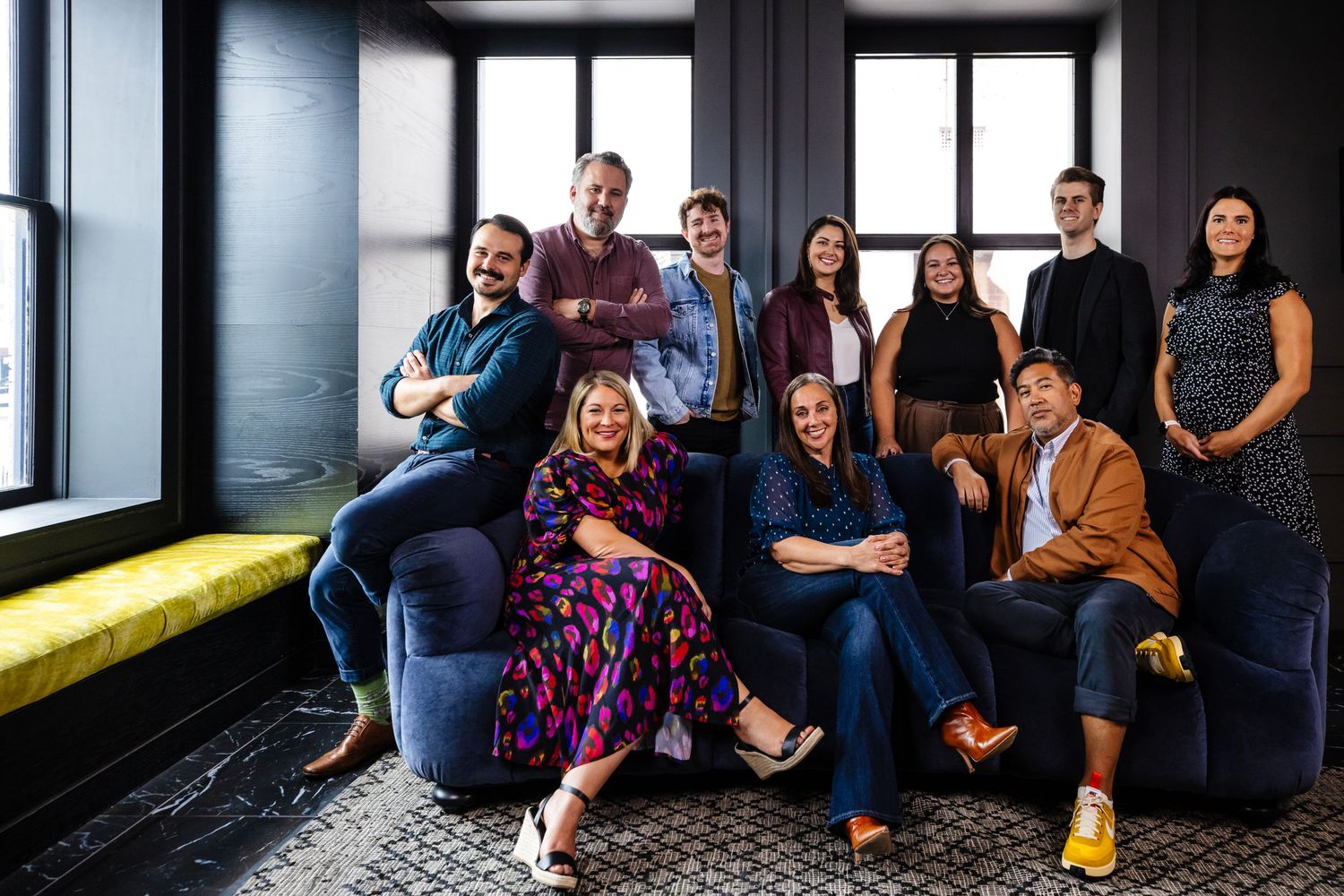 Group of coworkers in casual attire gather together in a modern office space for a team photo.