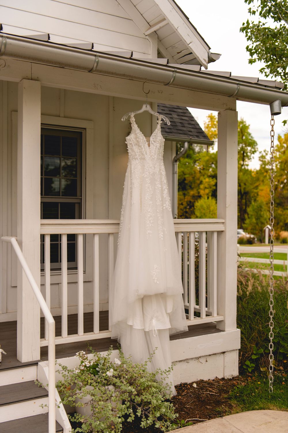 White wedding dresses hanging on hangers displayed on a white porch railing of a house with white siding.