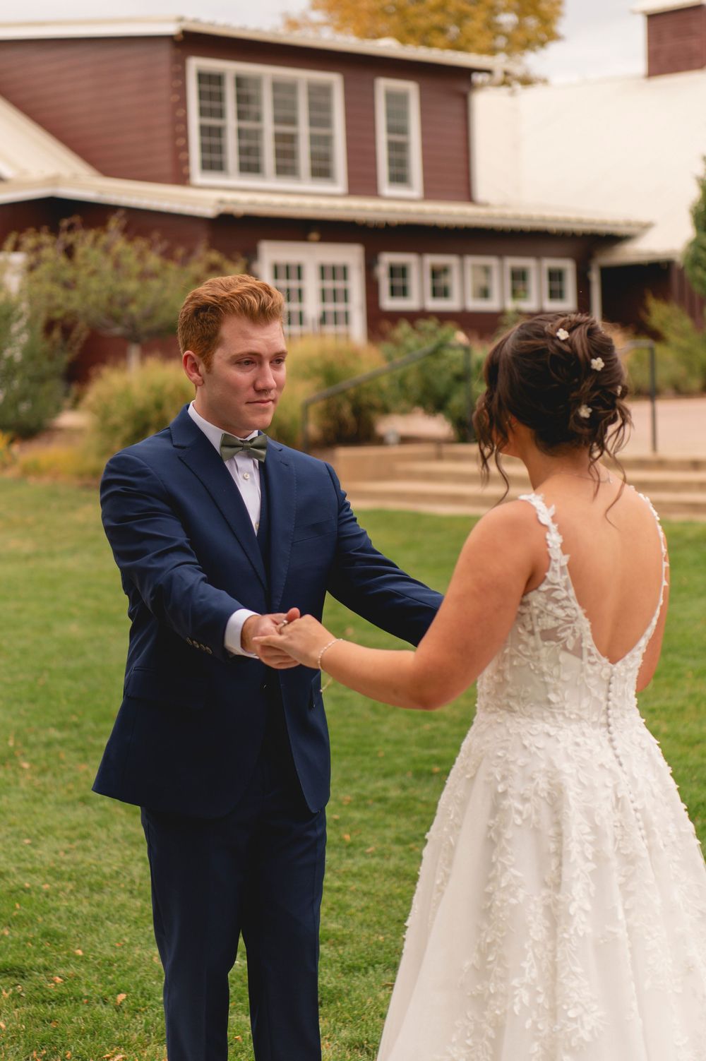 A couple shares their first look moment during an autumn wedding on a grassy lawn.