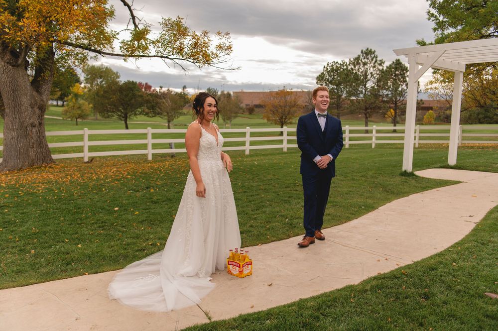 Couple stands on garden path with white pergola and autumn foliage at rustic outdoor wedding venue with white fencing.