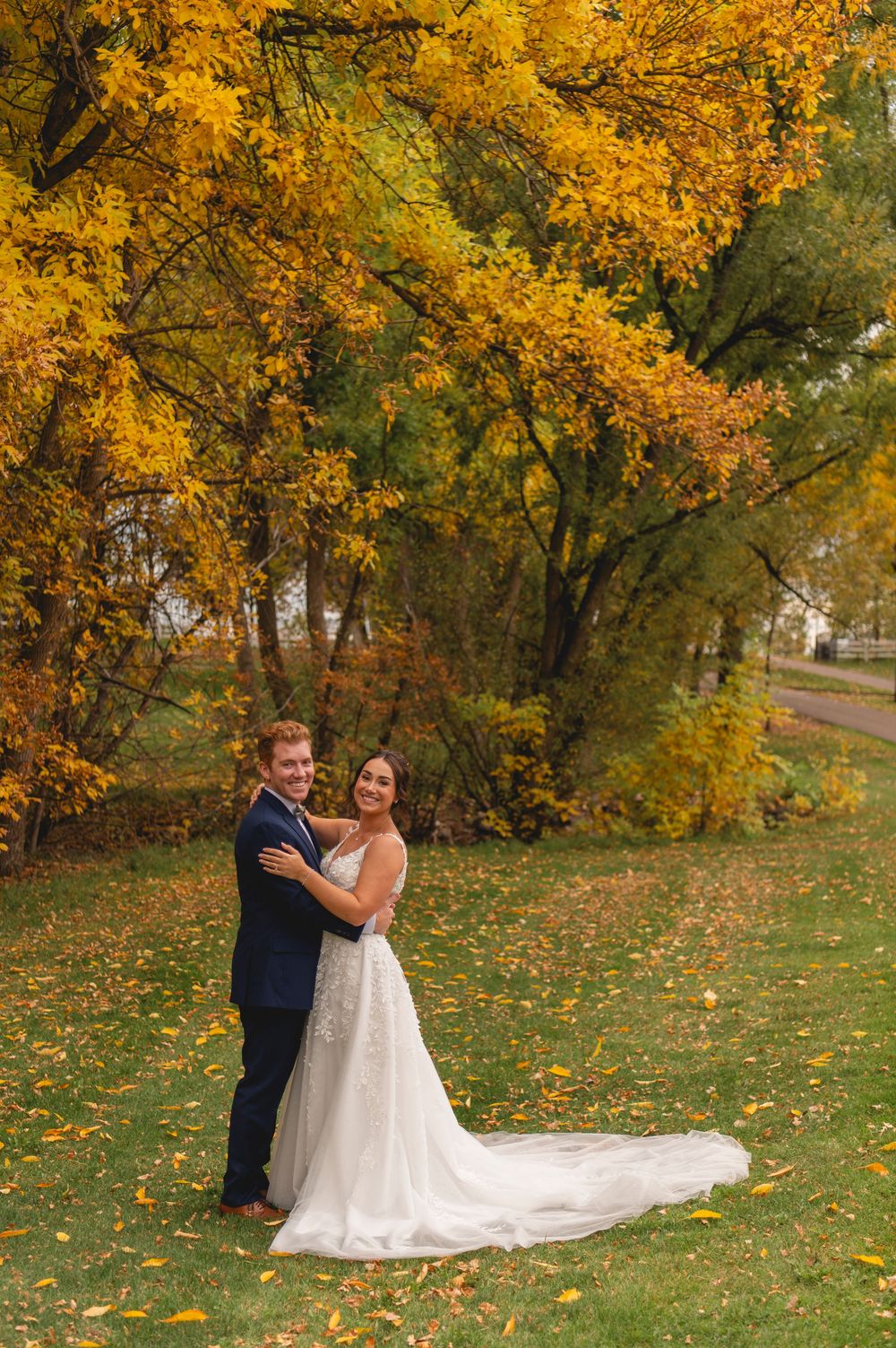 A couple shares a romantic autumn moment surrounded by golden foliage in a park setting.