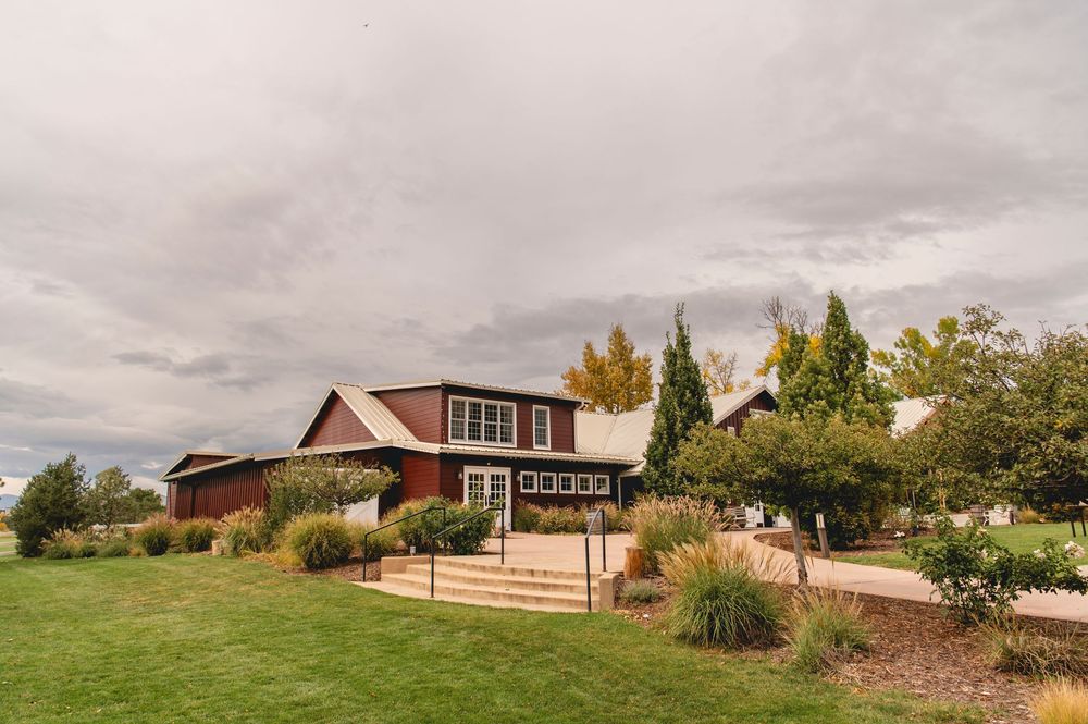 A panoramic view of a modern ranch-style house nestled in rolling green hills with cloudy skies overhead.