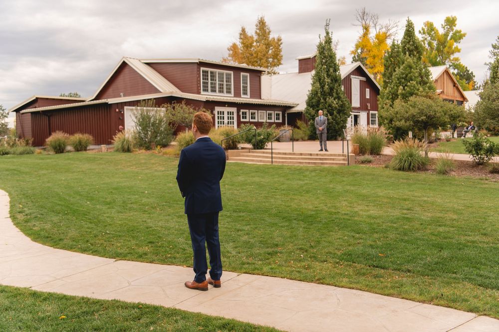 A person in a blue jacket walks across a grassy lawn near residential buildings on an autumn day.