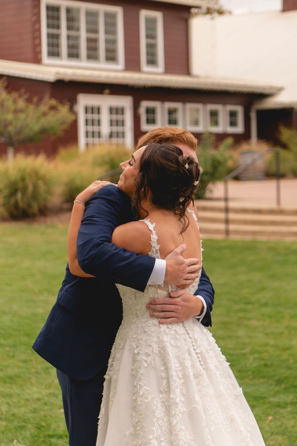 A romantic first look moment between newlyweds on a grassy lawn outside a red brick building.