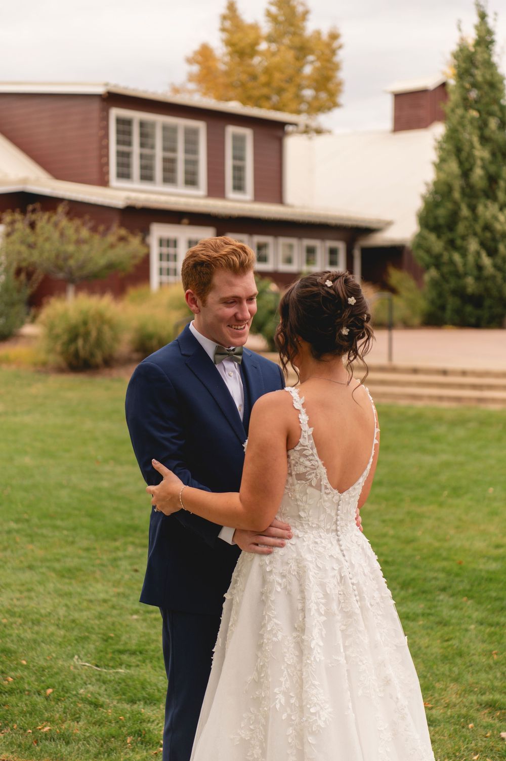 A couple shares a tender moment on their wedding day in a grassy outdoor setting wearing navy suit and white gown.