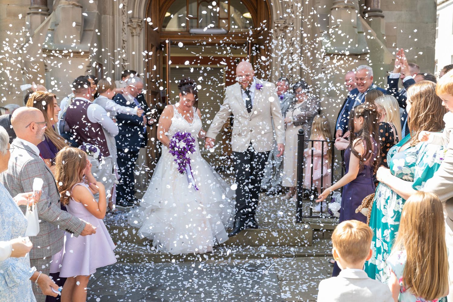 Wedding guests celebrate outside with confetti being thrown in the air during a joyous moment.