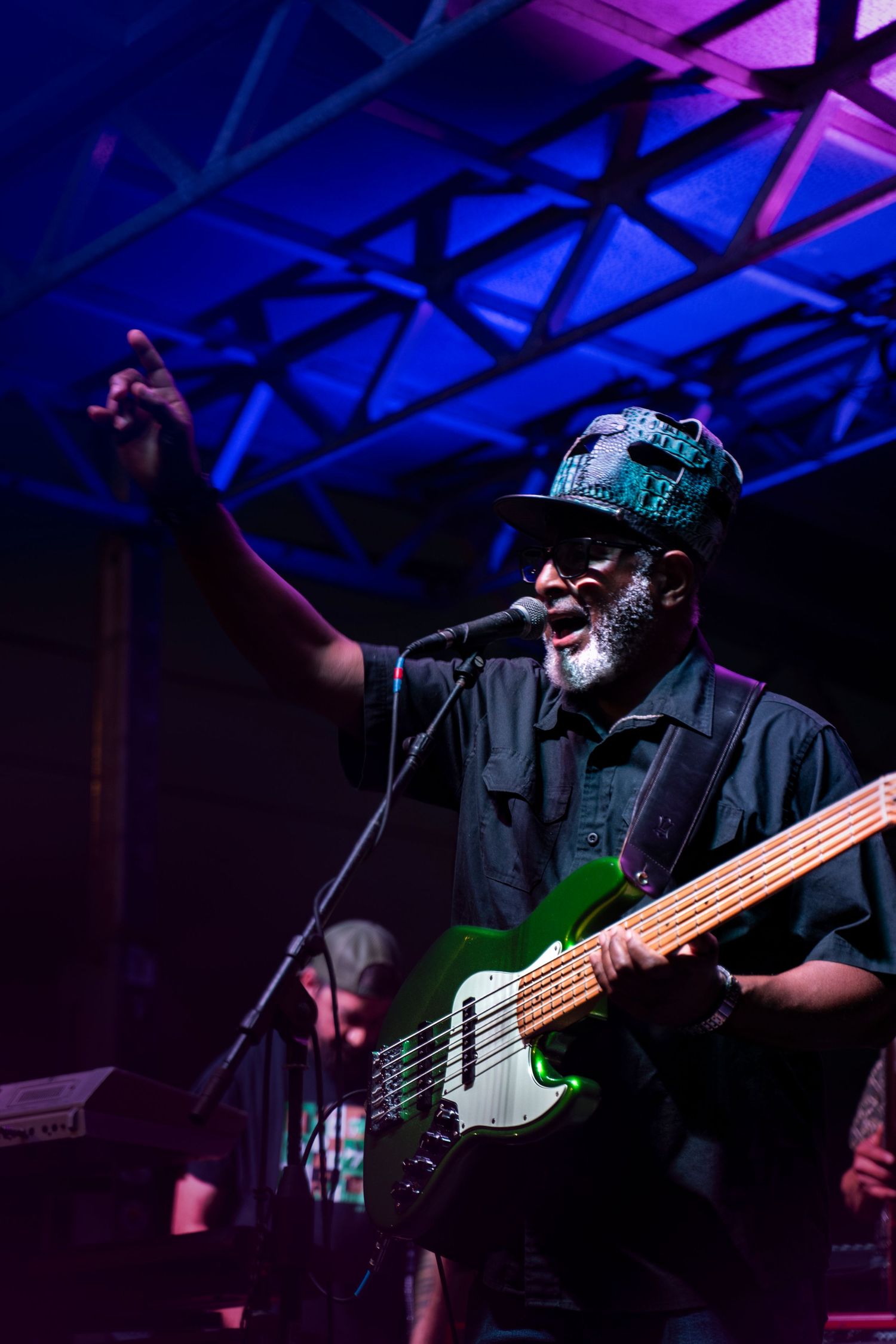 Bass player performs on stage with blue and purple lighting during live concert performance.