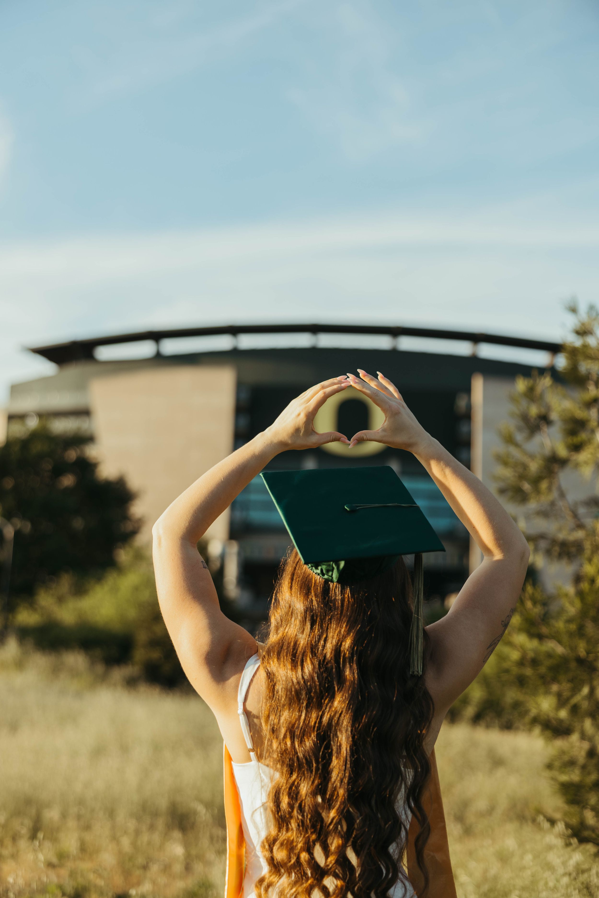 Graduate makes O shape with hands toward Oregon stadium during sunset photo session.