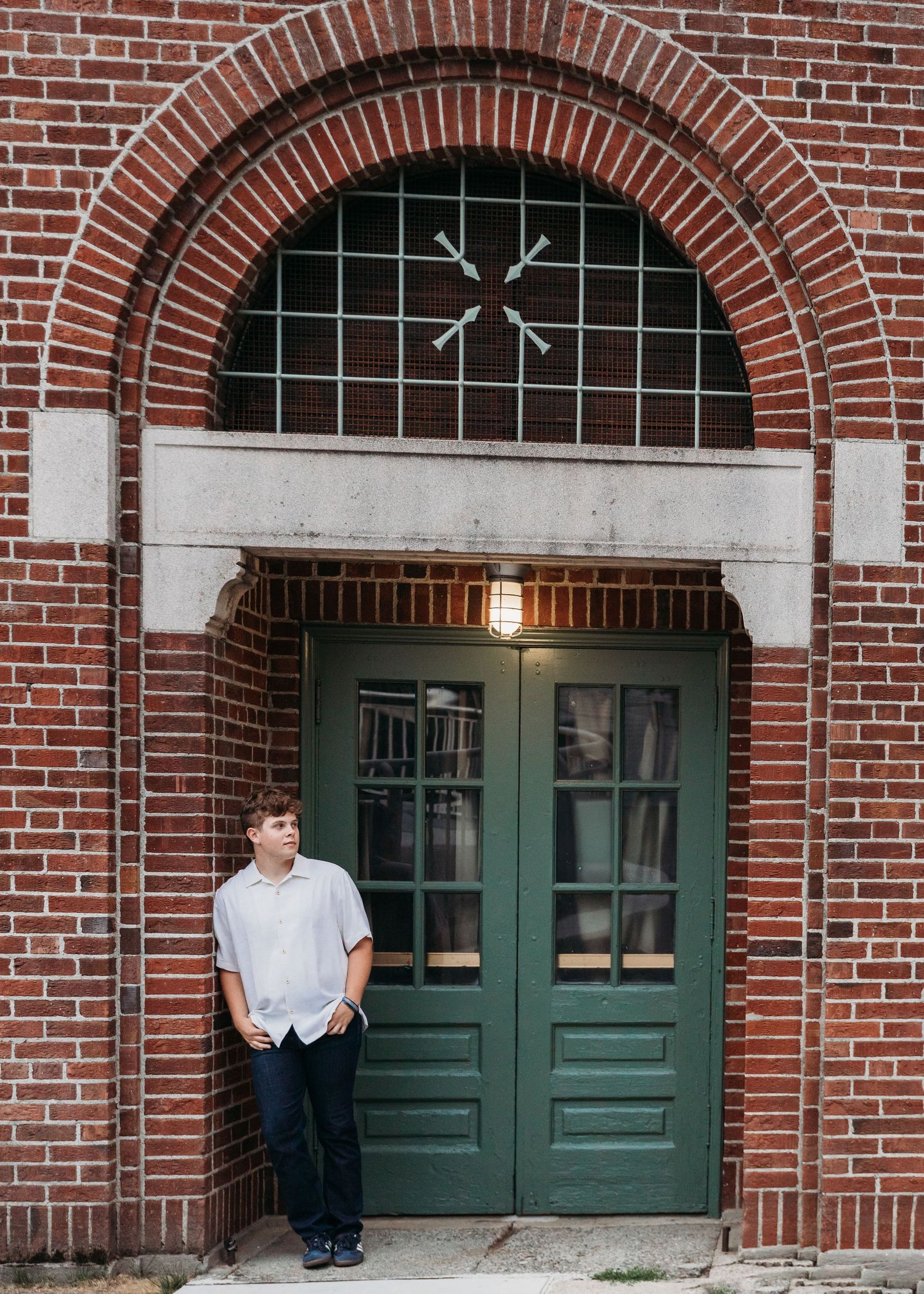 Person sitting on brick building steps with green doors and arched entryways in traditional architecture style.