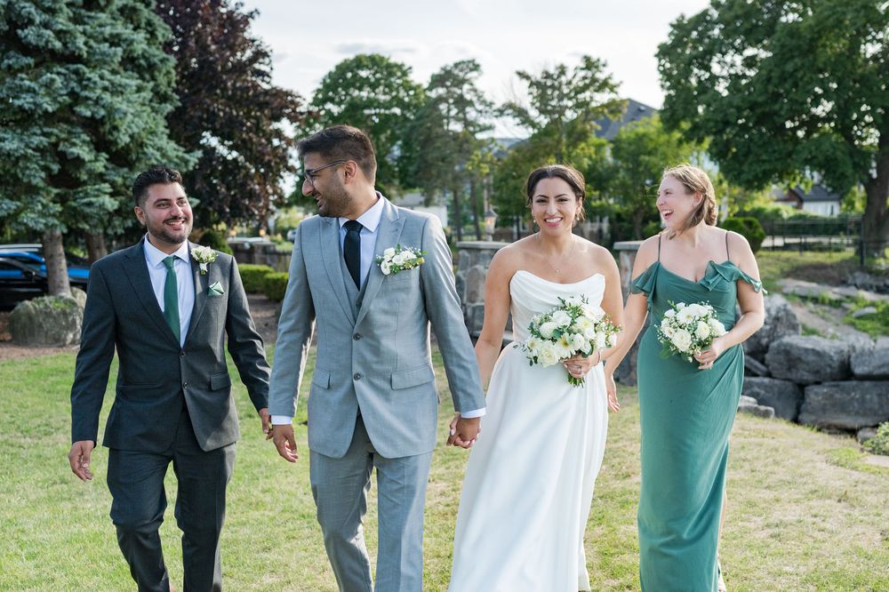 Wedding party members walk together outdoors wearing grey suits and seafoam green dresses.