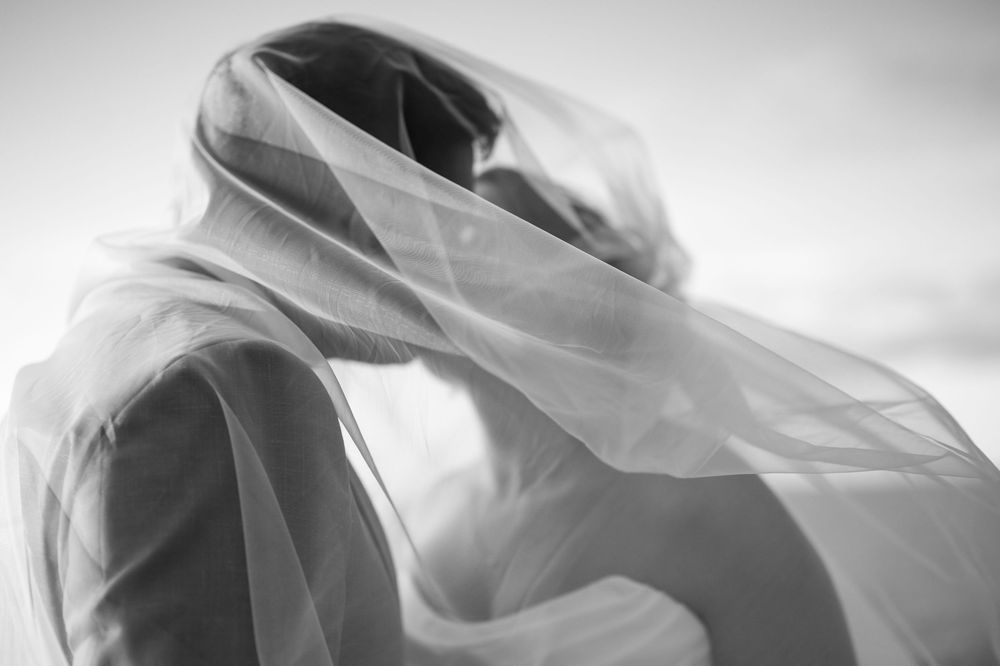 Flowing white wedding veil catches the breeze in an artistic black and white photograph.