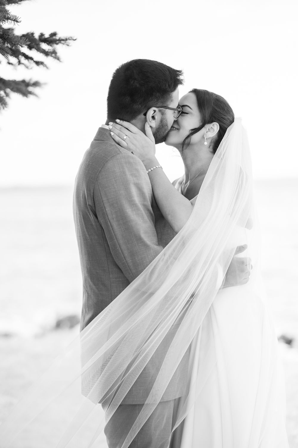 Black and white romantic portrait of a couple sharing an intimate moment under evergreen trees.