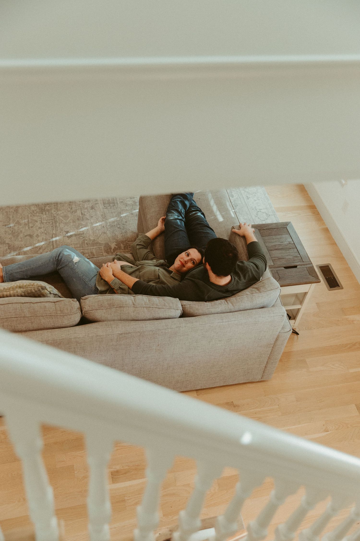 Someone relaxing on a gray couch viewed through white stair railings.