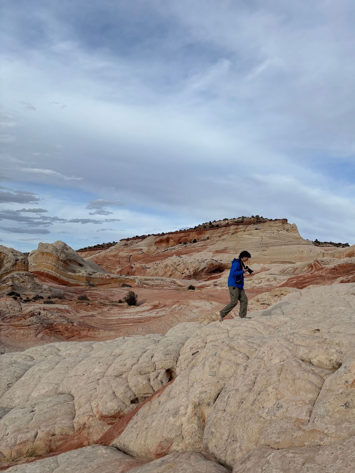 A hiker explores the dramatic red and white striped sandstone formations under cloudy skies in the American Southwest.
