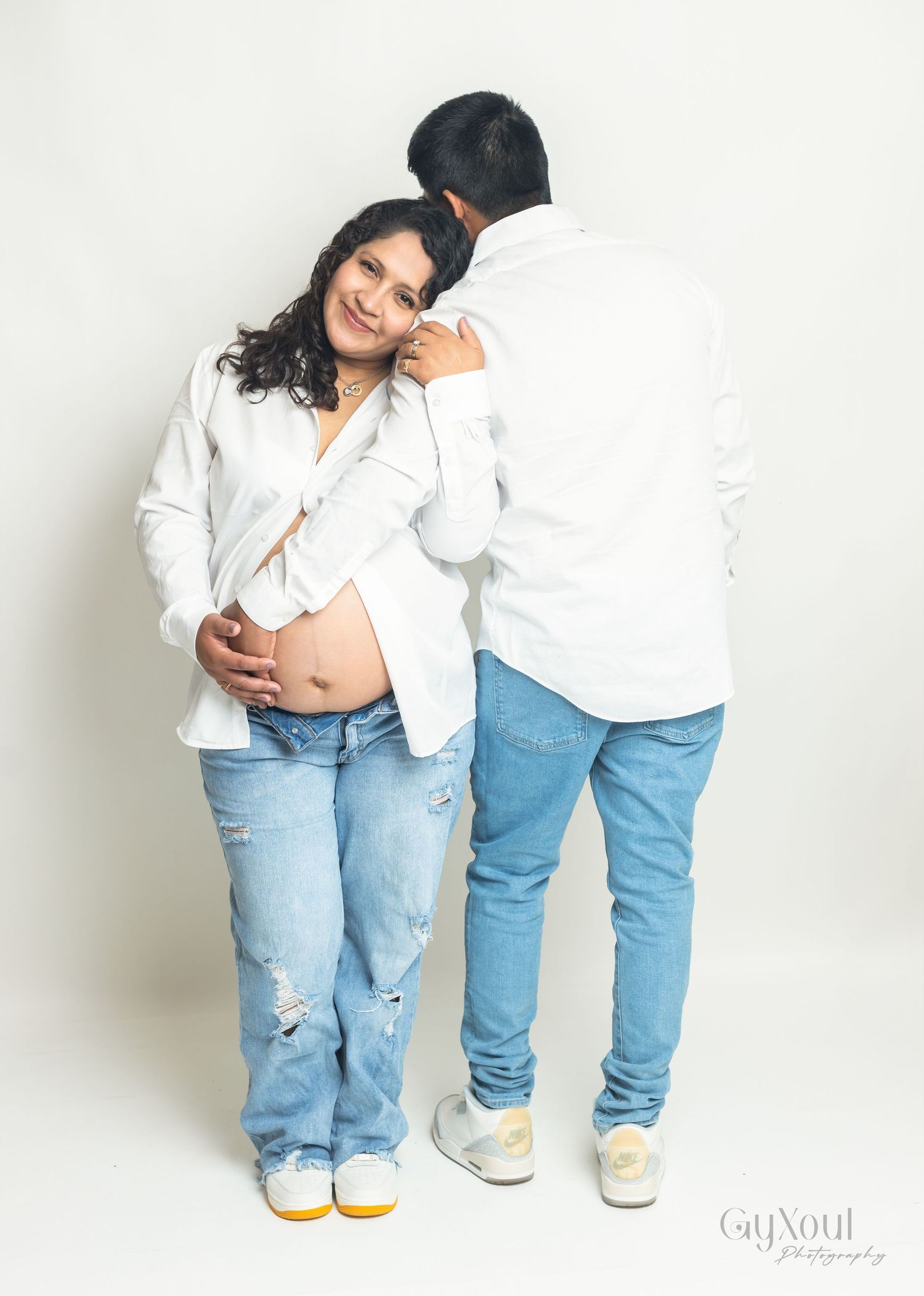Two people in matching light blue distressed jeans and white shirts pose playfully against a white background.