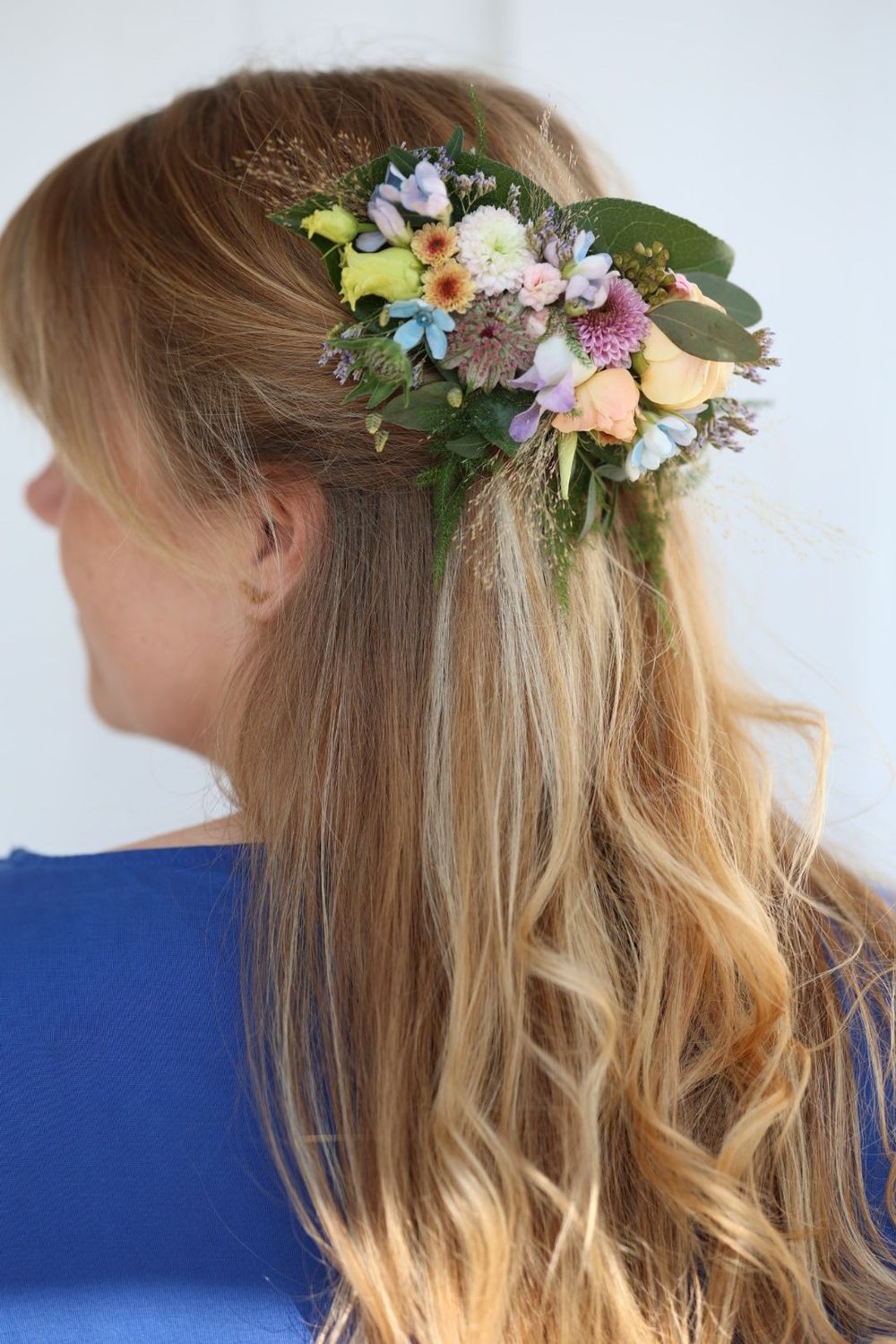 Woman with long blonde hair adorned with a beautiful floral hair piece featuring pastel flowers and greenery.