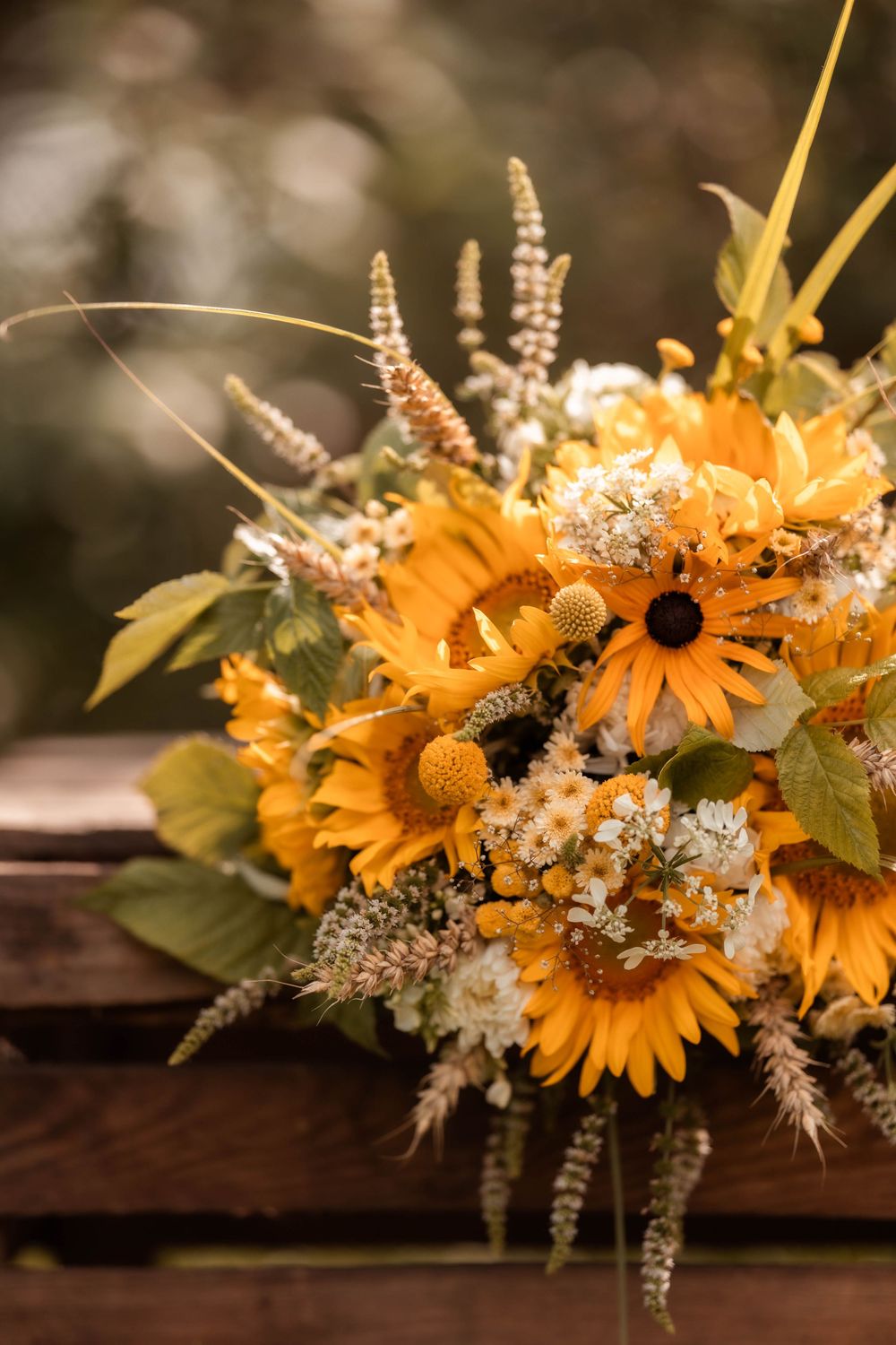 Rustic bouquet of sunflowers, white blooms, and wildgrasses on a wooden crate in warm autumn tones.