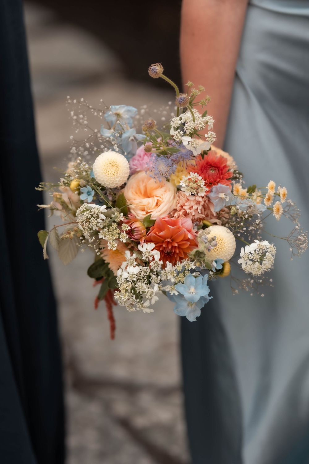 Bridesmaid holding a colorful wildflower wedding bouquet with dahlias, baby's breath, and blue blooms in a light blue dress.