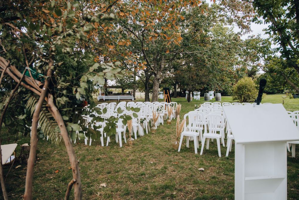 Outdoor wedding ceremony venue with white chairs on lawn, wooden lectern, and autumn trees in background.