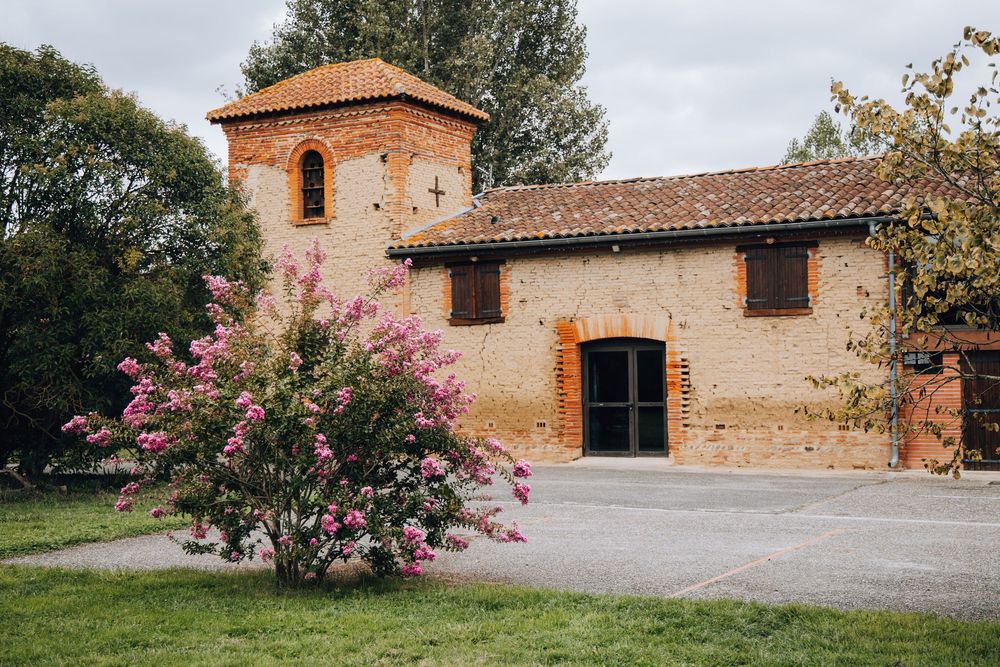 Charming rustic brick wedding venue with tower, terracotta roof tiles, and vibrant pink flowering shrub.